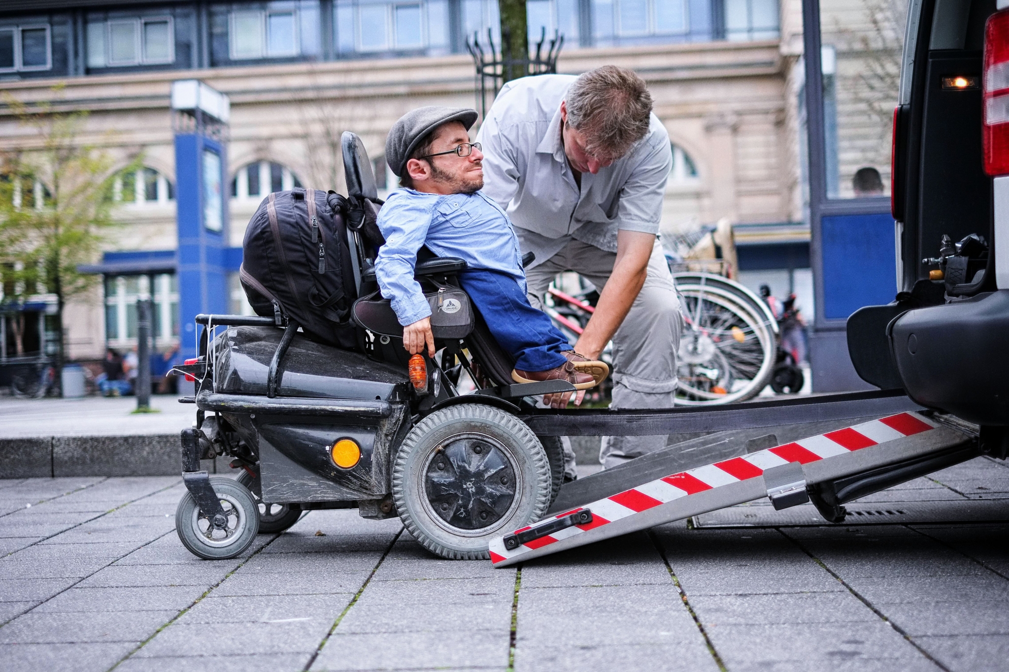 Ein Rollstuhlfahrer gelangt über eine kleine Rampe in das Rollstuhltaxi. Neben ihm steht ein Taxifahrer, der ihm beim Einsteigen hilft.