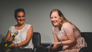 Ein Podium der Veranstaltung "Inklusion im Fernsehen" der Grimme Akademie bei RTL in Köln. Auf dem Podium sitzen zwei Frauen, eine der beiden hat das Down-Syndrom. Beide halten ein Mikrofon in der Hand und lächeln in die Kamera.