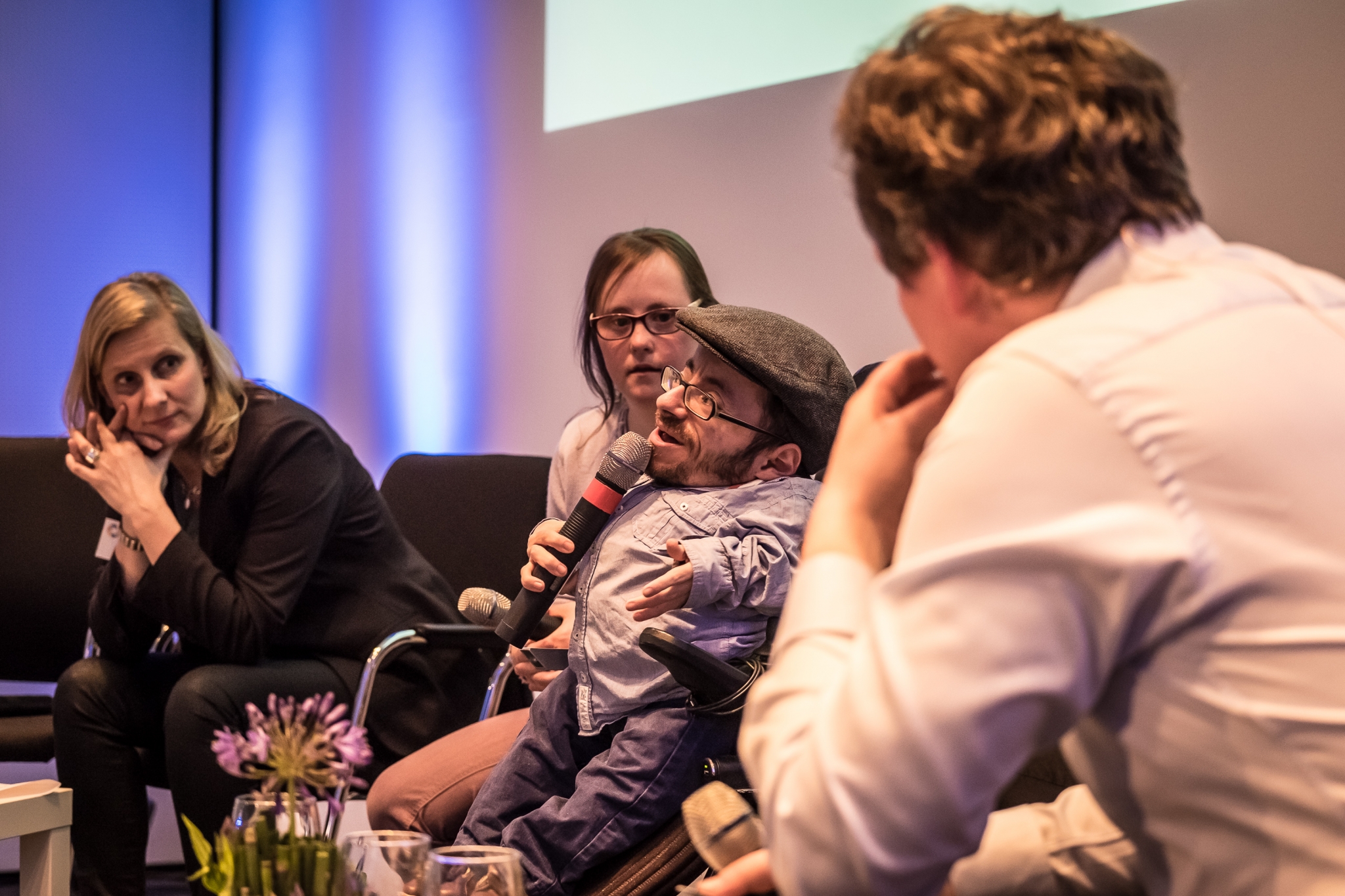 Podiumsgäste auf der Veranstaltung "Inklusion im Fernsehen" der Grimme Akademie bei RTL in Köln. Es spricht ein kleinwüchsiger Rollstuhlfahrer ins Mikro. Neben ihm sitzen eine Frau mit Down-Syndrom und eine nicht behinderte Frau. Der Moderator ist im Vordergrund zu sehen.